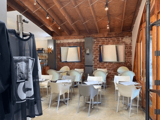 The café inside Anastasia Boutique: white tables and chairs against an exposed brick wall hung with framed artwork, beneath a timber ceiling, with a garment on a rail at left